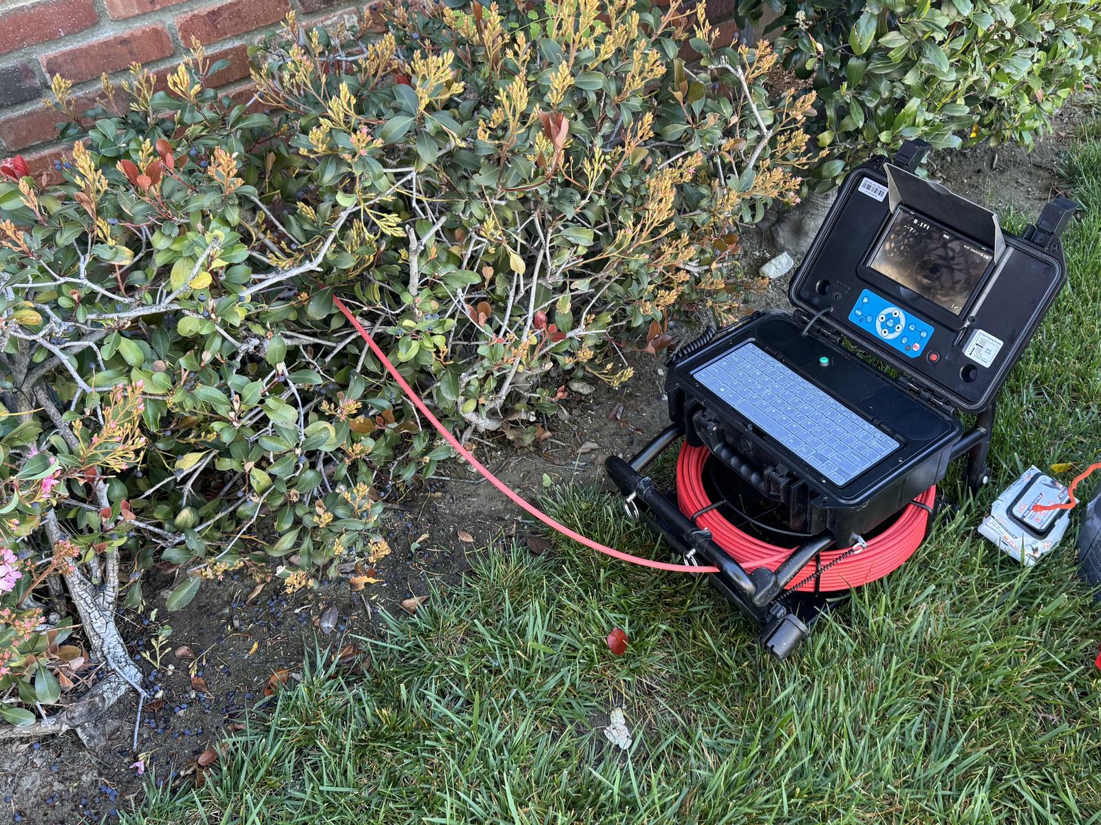 Sewer inspection camera reel and monitor staged on a lawn beside a residential cleanout