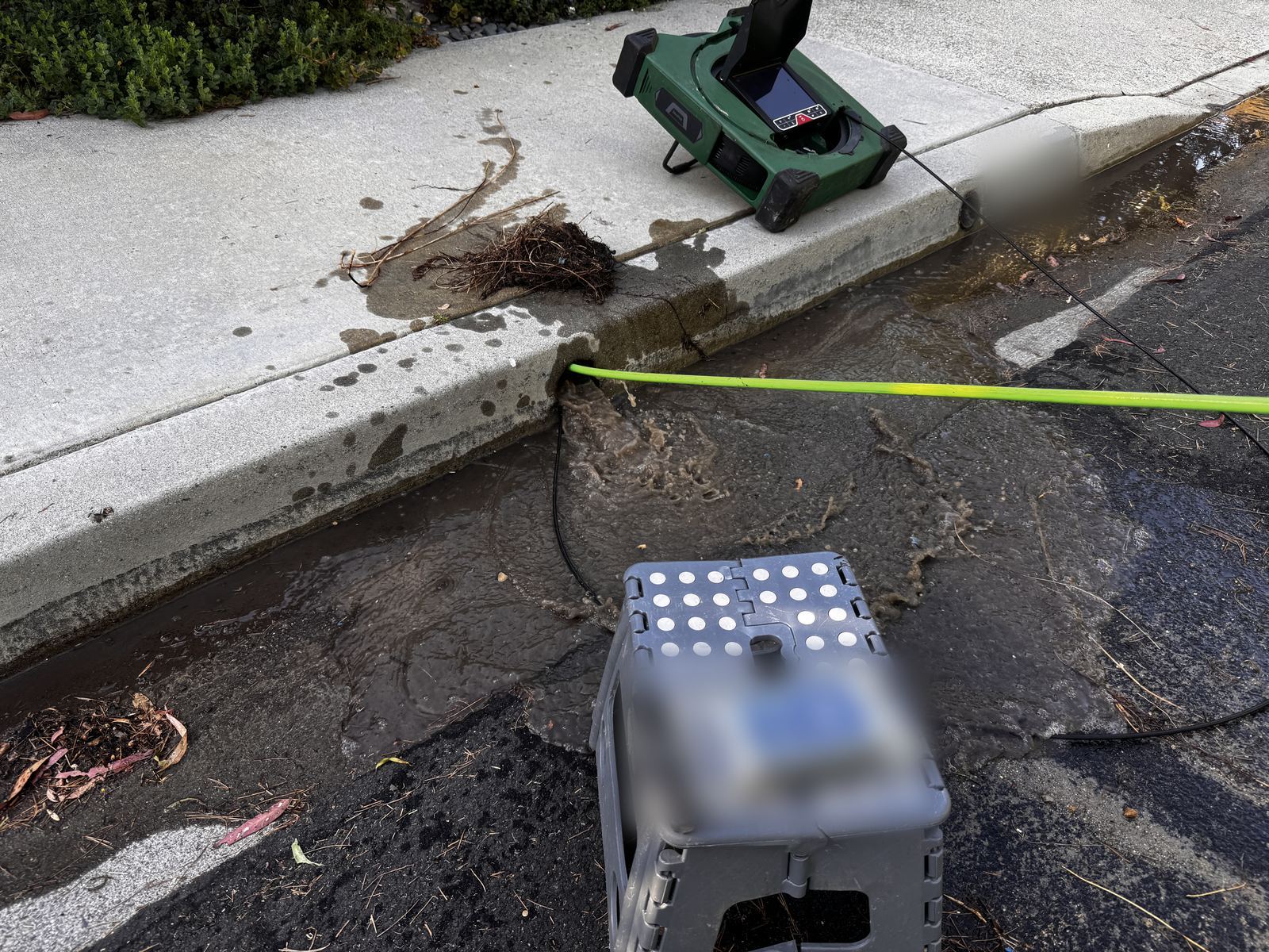 Muddy backed-up water rushing out of a curb outlet after a yard drain blockage is cleared