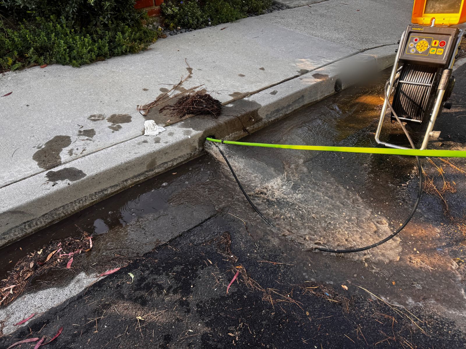 Water flowing out of a curb drain outlet into the gutter after the line is cleared